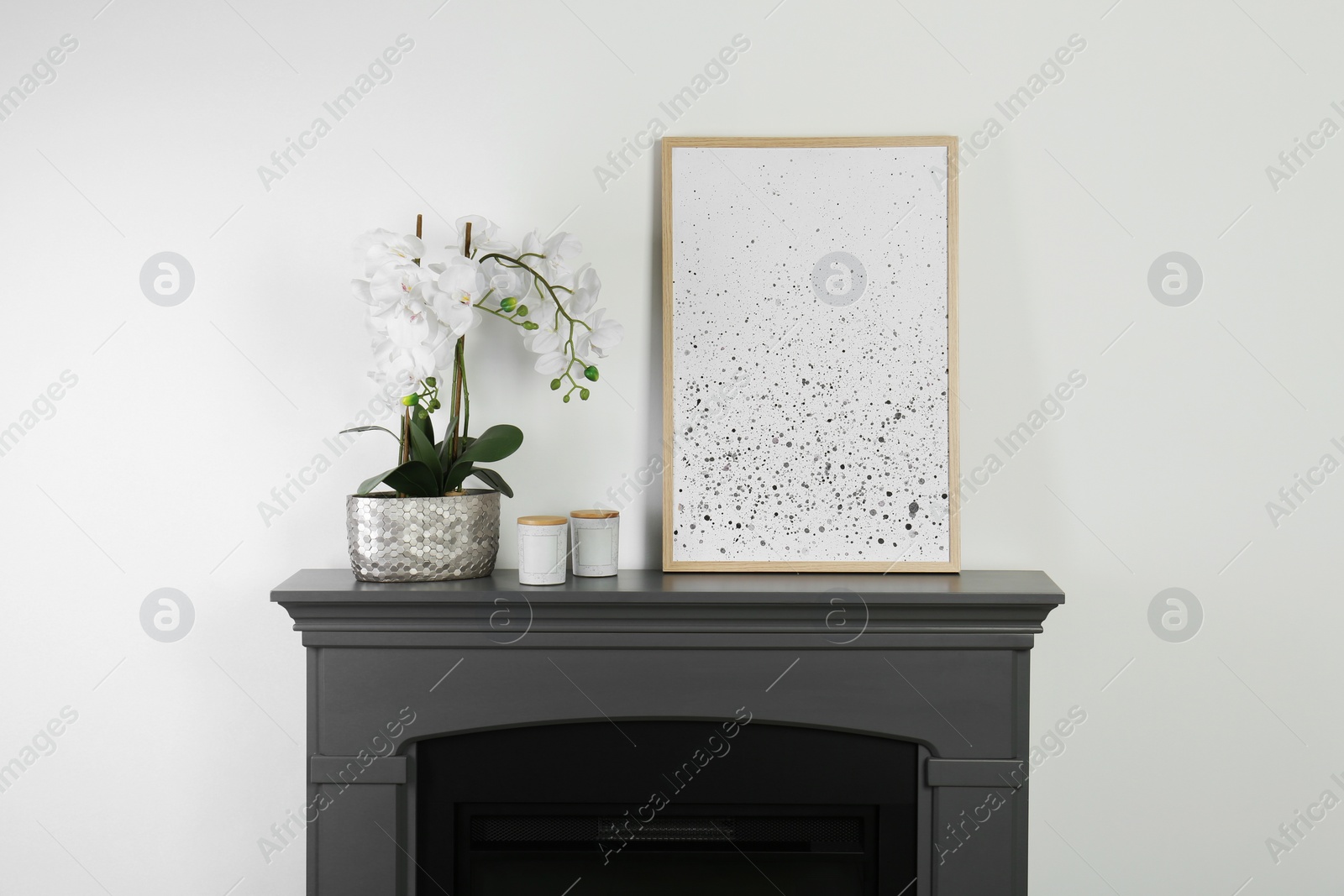 Photo of Picture frame, candles and orchid on fireplace near white wall indoors. Interior design