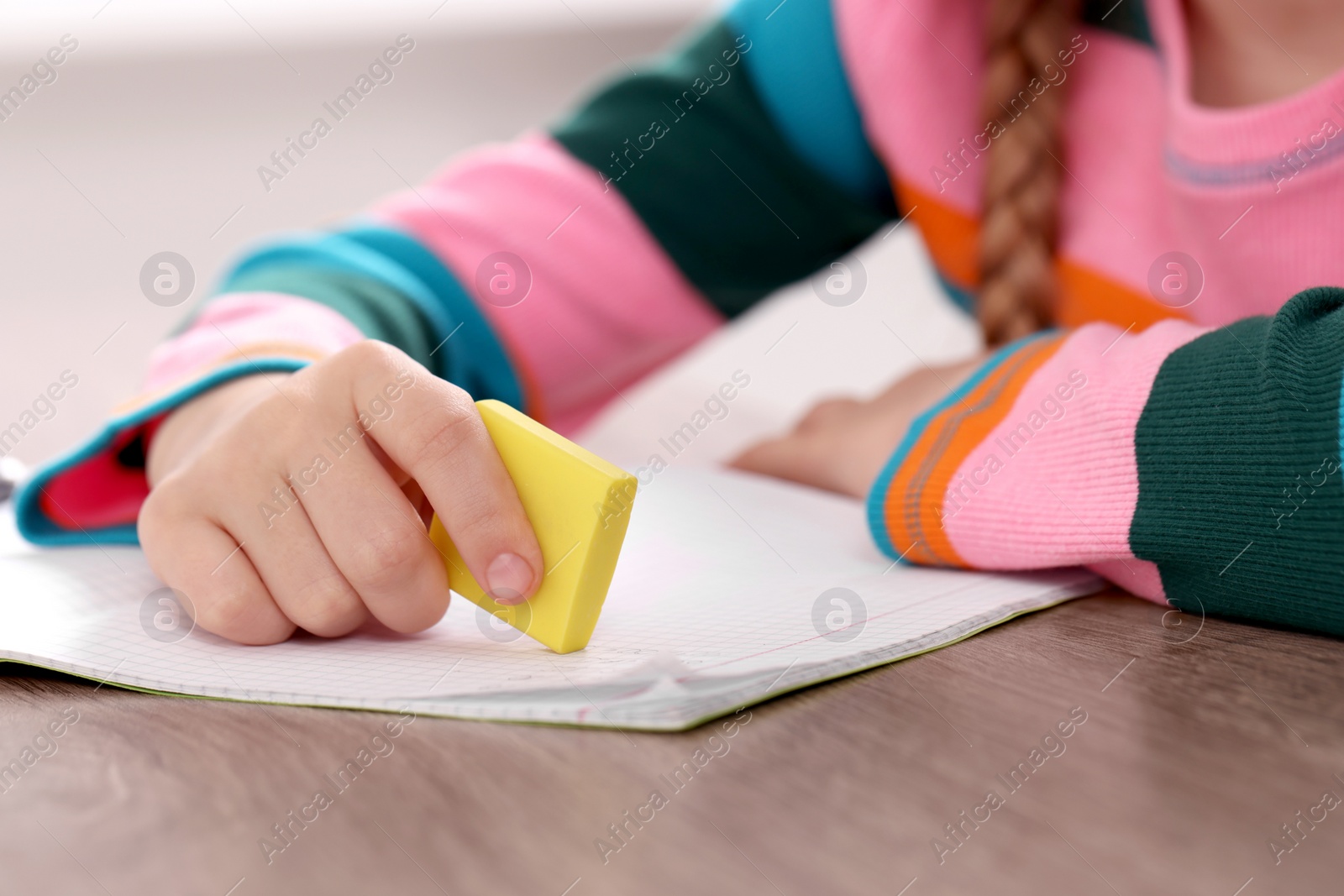 Photo of Girl erasing mistake in her homework at wooden table, closeup