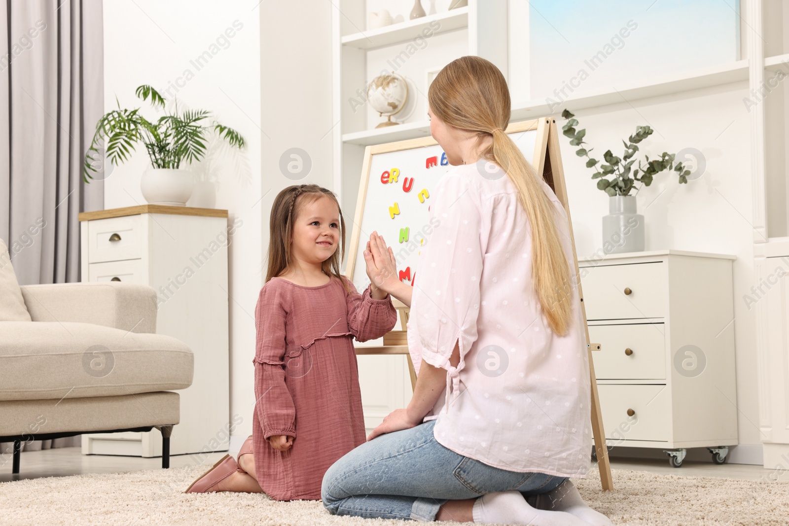 Photo of Mom and daughter giving each other high five while learning alphabet with magnetic letters at home