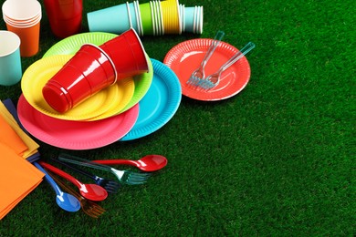 Photo of Disposable tableware on green artificial grass. Space for text
