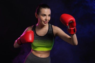 Photo of Portrait of beautiful woman wearing boxing gloves training in color lights on black background