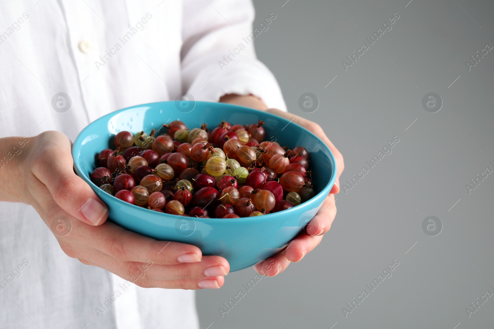 Photo of Woman holding bowl full of ripe gooseberries on light background closeup. Space for text