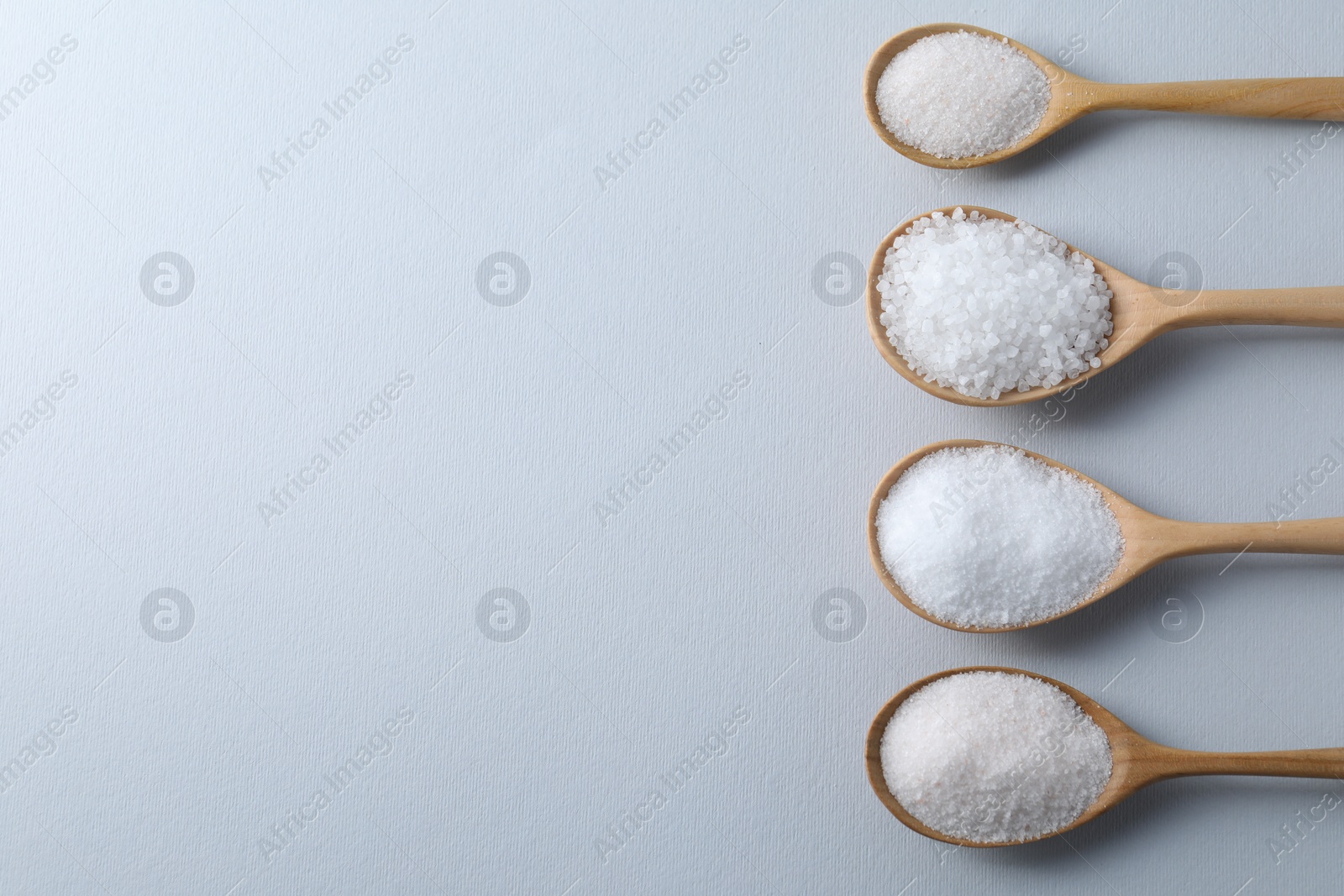 Photo of Organic white salt in spoons on light grey background, flat lay. Space for text