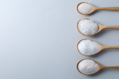 Photo of Organic white salt in spoons on light grey background, flat lay. Space for text