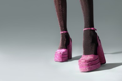Photo of Woman wearing pink high heeled shoes with platform and square toes on light grey background, closeup. Space for text