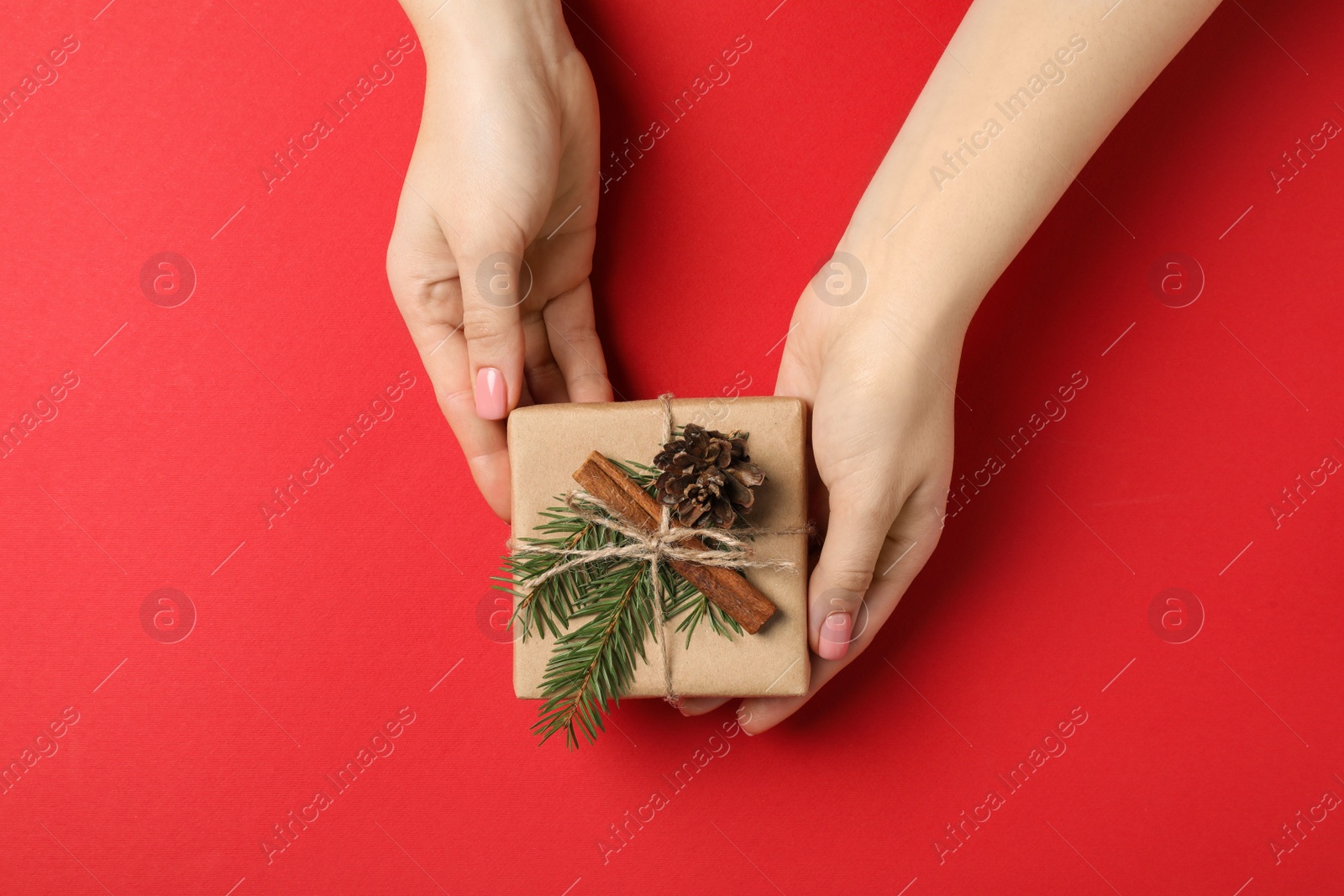 Photo of Christmas present. Woman holding beautifully wrapped gift box on red background, top view