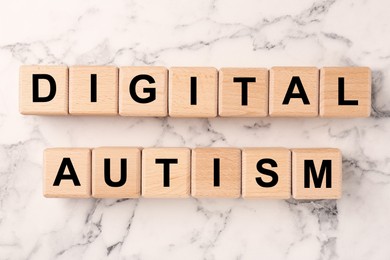 Photo of Phrase Digital Autism made of wooden cubes on white marble table, top view