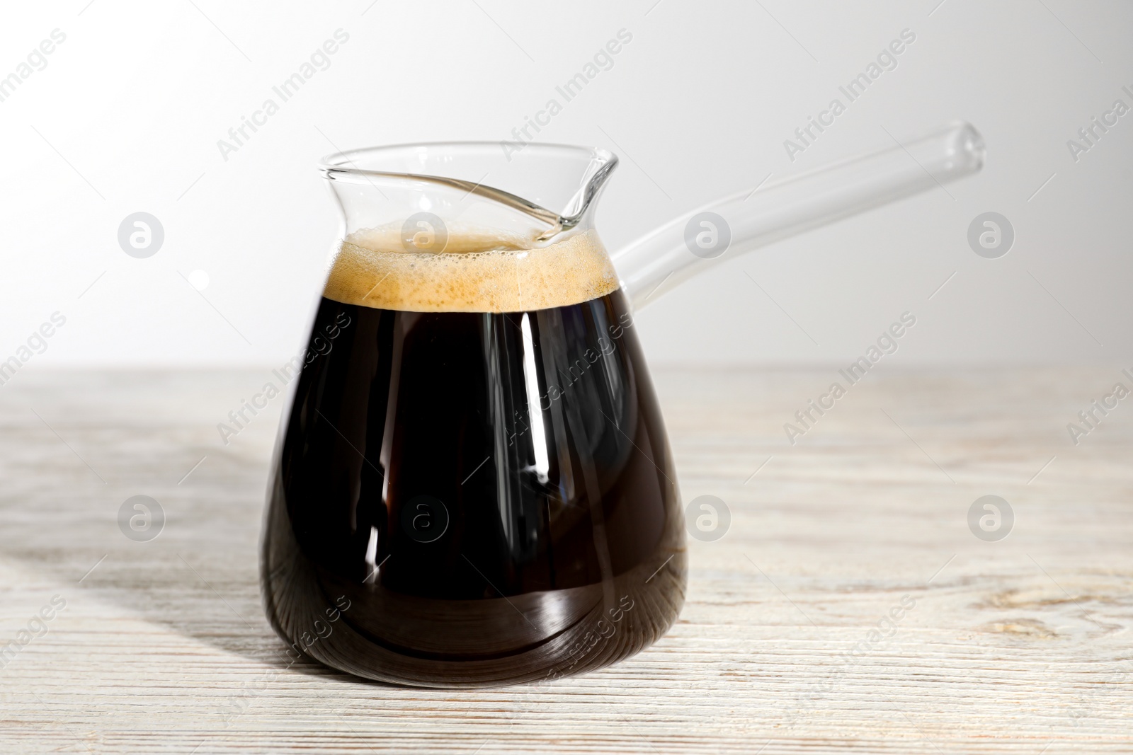 Photo of Glass turkish coffee pot with hot drink on wooden table