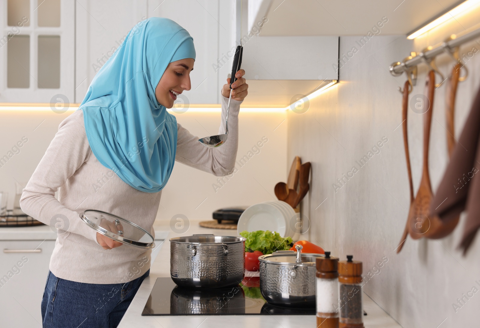 Photo of Muslim woman cooking dish in saucepan on cooktop indoors