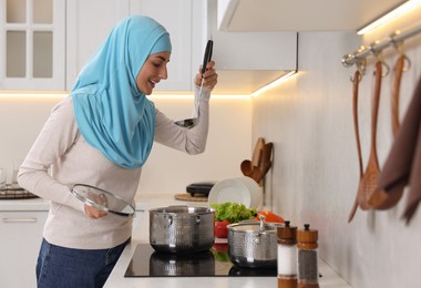 Muslim woman cooking dish in saucepan on cooktop indoors