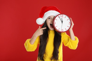 Photo of Girl in Santa hat with clock on red background. New Year countdown