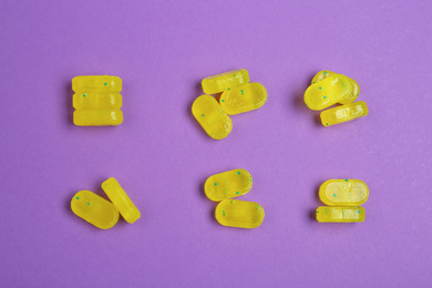 Tasty lemon drops on purple background, flat lay