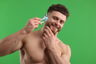 Handsome man applying lotion onto his face on green background