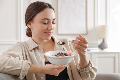 Photo of Woman eating tasty granola with fresh berries and yogurt at home