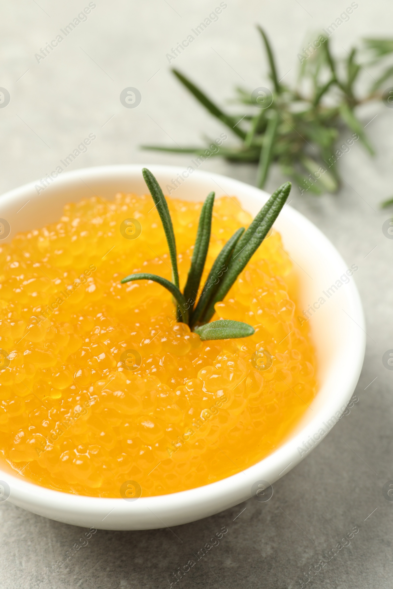 Photo of Fresh pike caviar in bowl and rosemary on light grey table, closeup