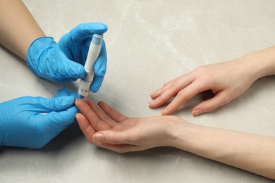 Diabetes. glucose testing. Doctor using lancet pen at light table, closeup