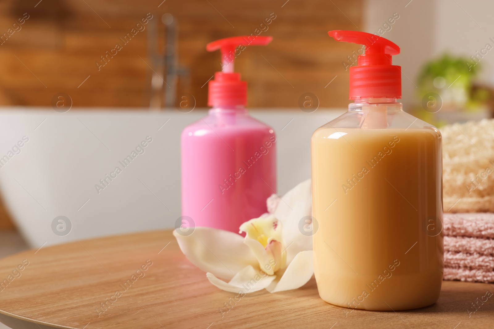 Photo of Dispensers of liquid soap and orchid flower on wooden table in bathroom, space for text