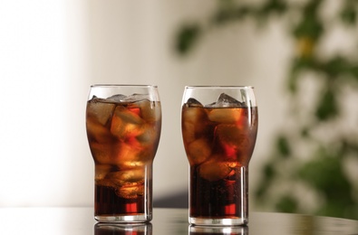 Glasses of cola with ice on table against blurred background