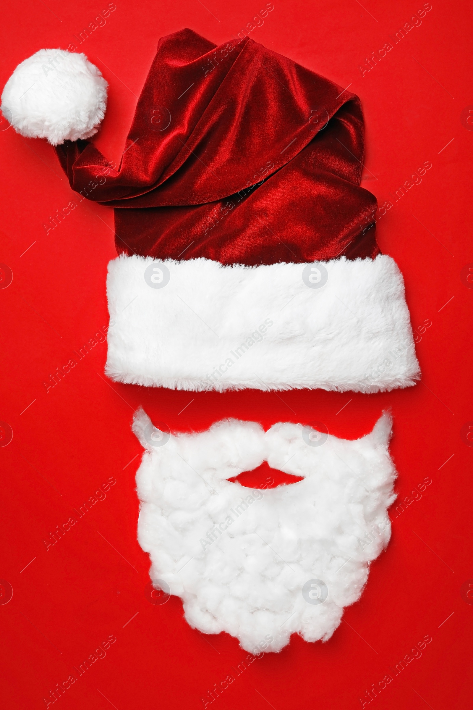 Photo of Santa Claus hat with white beard on red background, flat lay