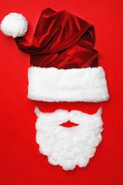 Santa Claus hat with white beard on red background, flat lay