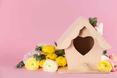 Stylish bird house and fresh flowers on pink background. Space for text