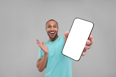 Surprised man showing smartphone in hand on light grey background, selective focus. Mockup for design