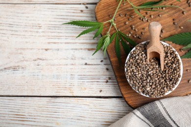 Photo of Organic hemp seeds and leaves on white wooden table, flat lay. Space for text