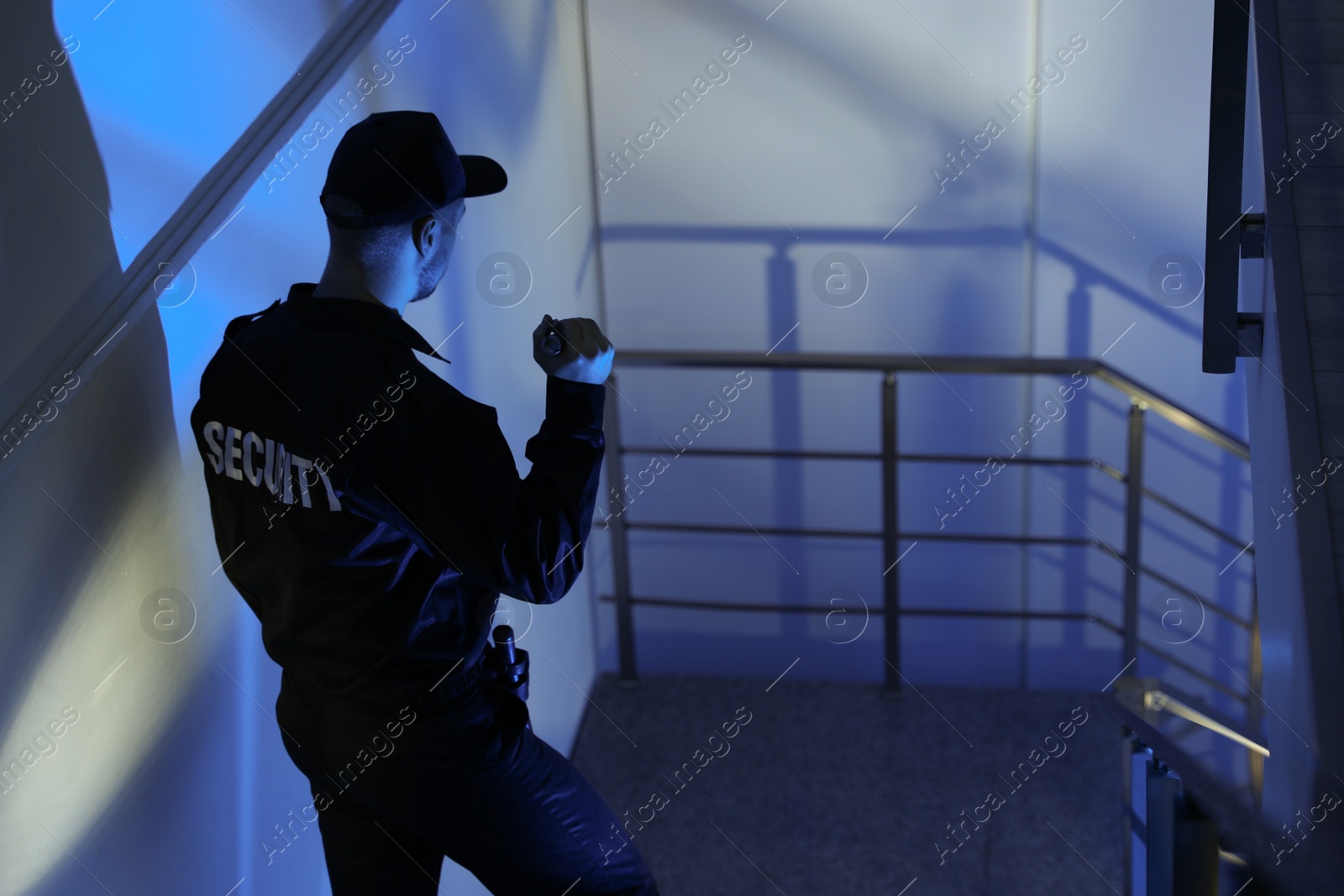 Photo of Male security guard with flashlight on stairs in darkness