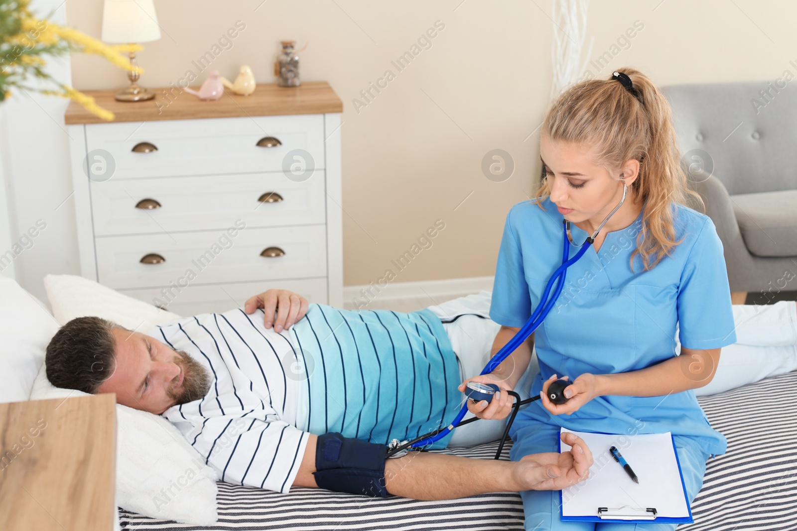Photo of Female medical assistant measuring male patient blood pressure during home visit
