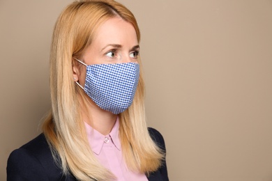 Photo of Woman wearing handmade cloth mask on beige background, space for text. Personal protective equipment during COVID-19 pandemic