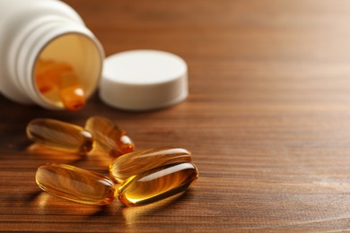 Photo of Dietary supplement capsules on wooden table, closeup. Space for text