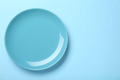 Photo of Empty ceramic plate on light blue background, top view. Space for text