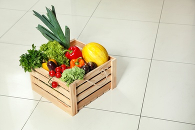 Photo of Wooden crate with fresh vegetables on floor. Space for text