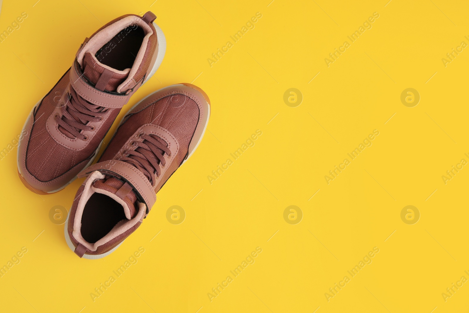 Photo of Pair of stylish kid's sneakers on yellow background, top view. Space for text