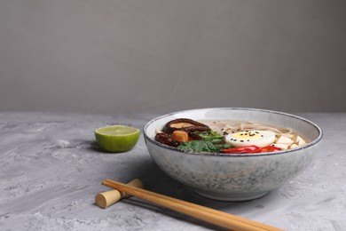 Photo of Delicious vegetarian ramen served on grey table, space for text. Noodle soup