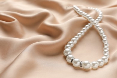 Photo of Elegant necklace with pearls on beige silk, closeup. Space for text