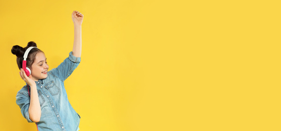 Little girl listening to music with headphones on yellow background, space for text. Banner design