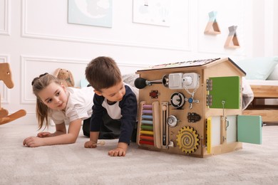 Photo of Little boy and girl playing with busy board house on floor in room