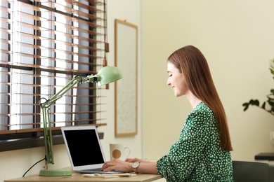 Young woman using laptop at table indoors. Space for text