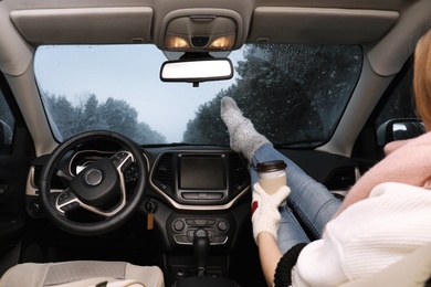 Woman in warm socks with coffee resting inside car, closeup