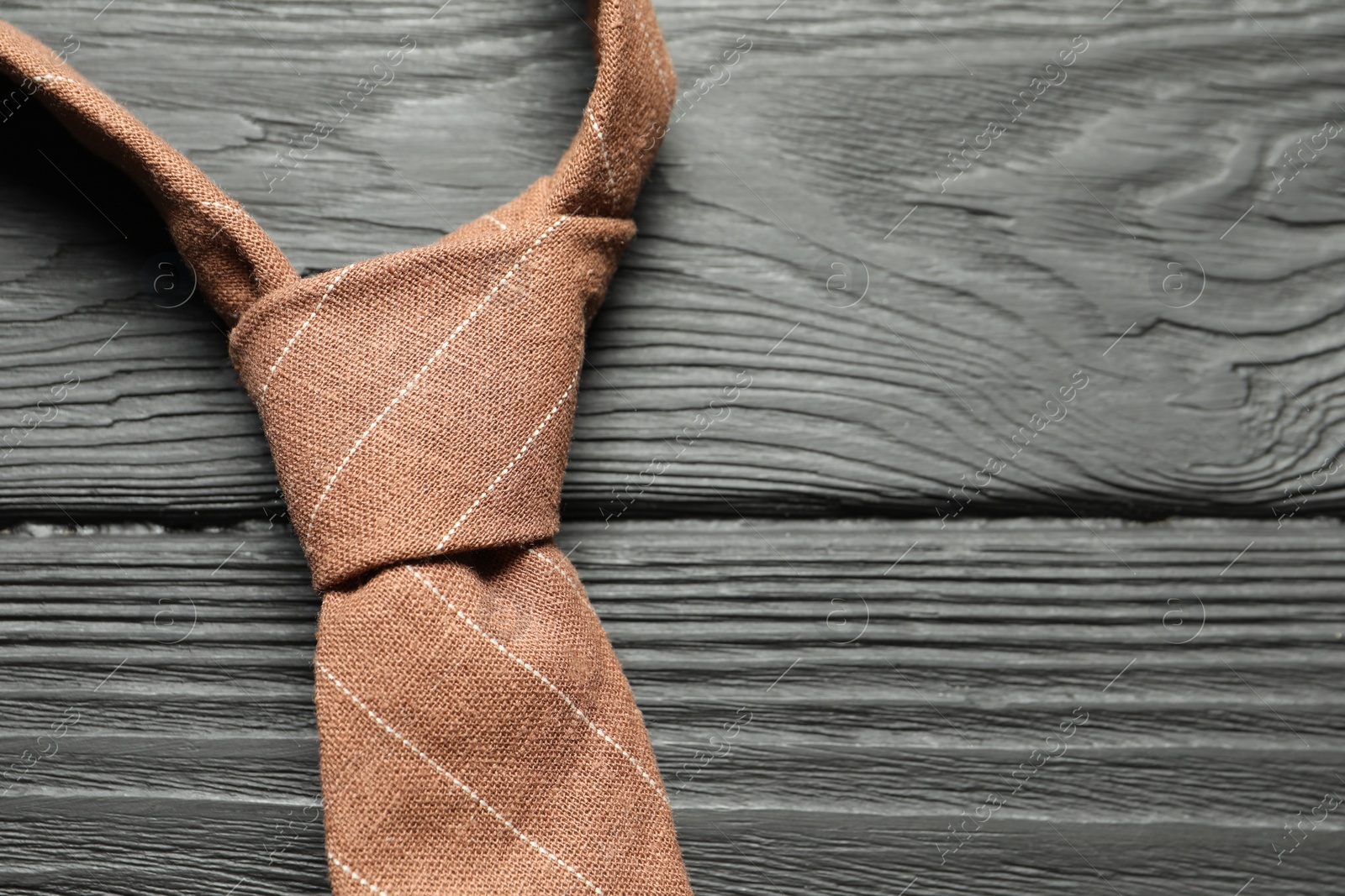 Photo of One striped necktie on black wooden table, top view. Space for text