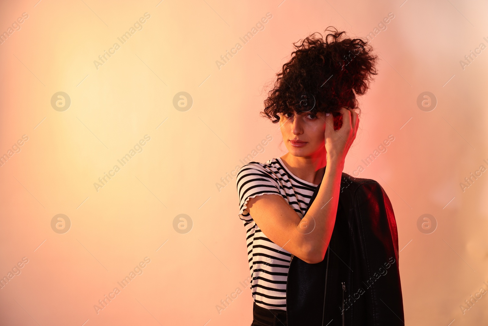 Photo of Beautiful young woman in black leather jacket posing on color background in neon lights. Space for text