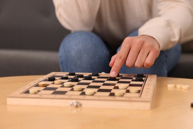 Photo of Woman playing checkers at wooden table, closeup