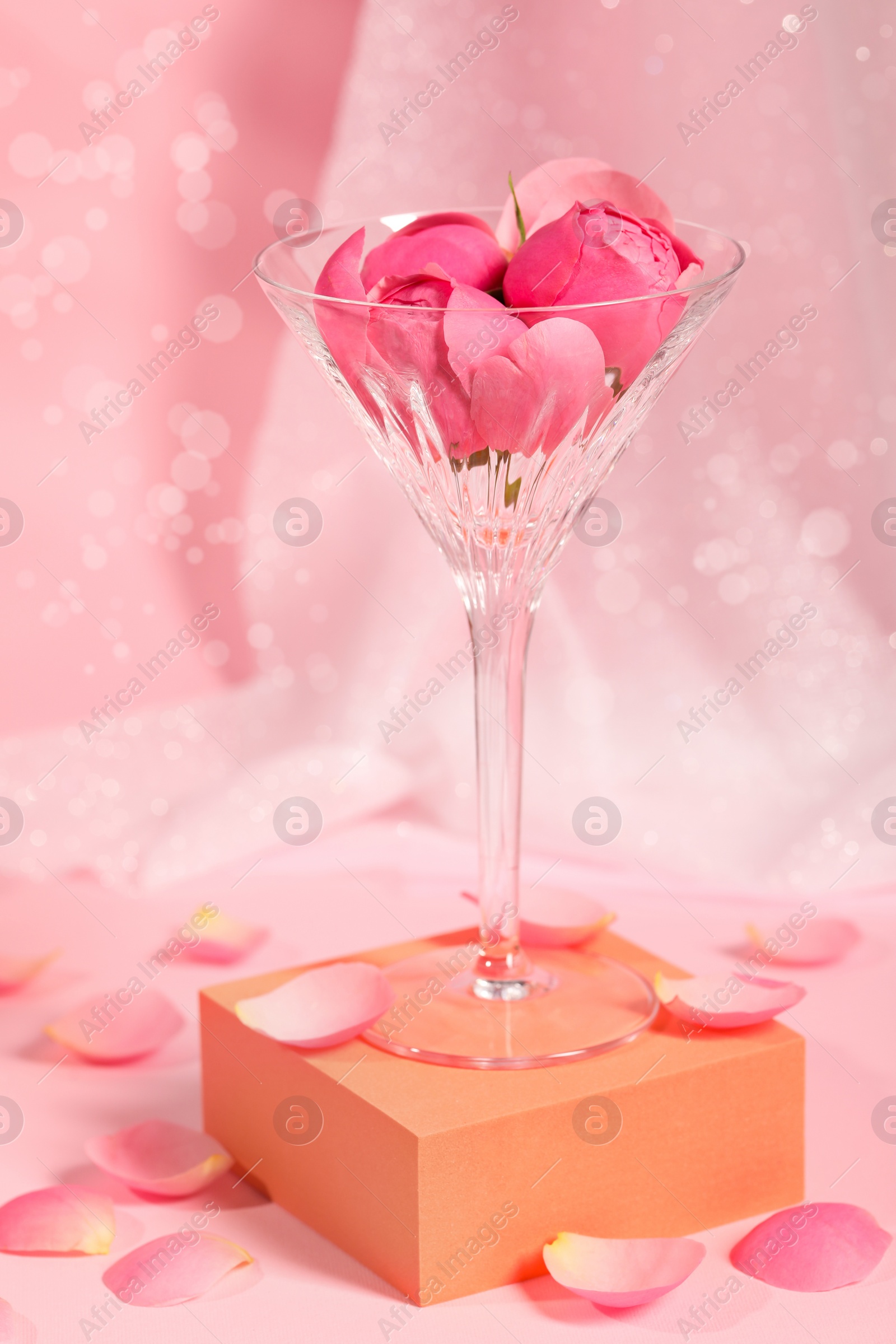 Photo of Martini glass with flowers and petals on pink background