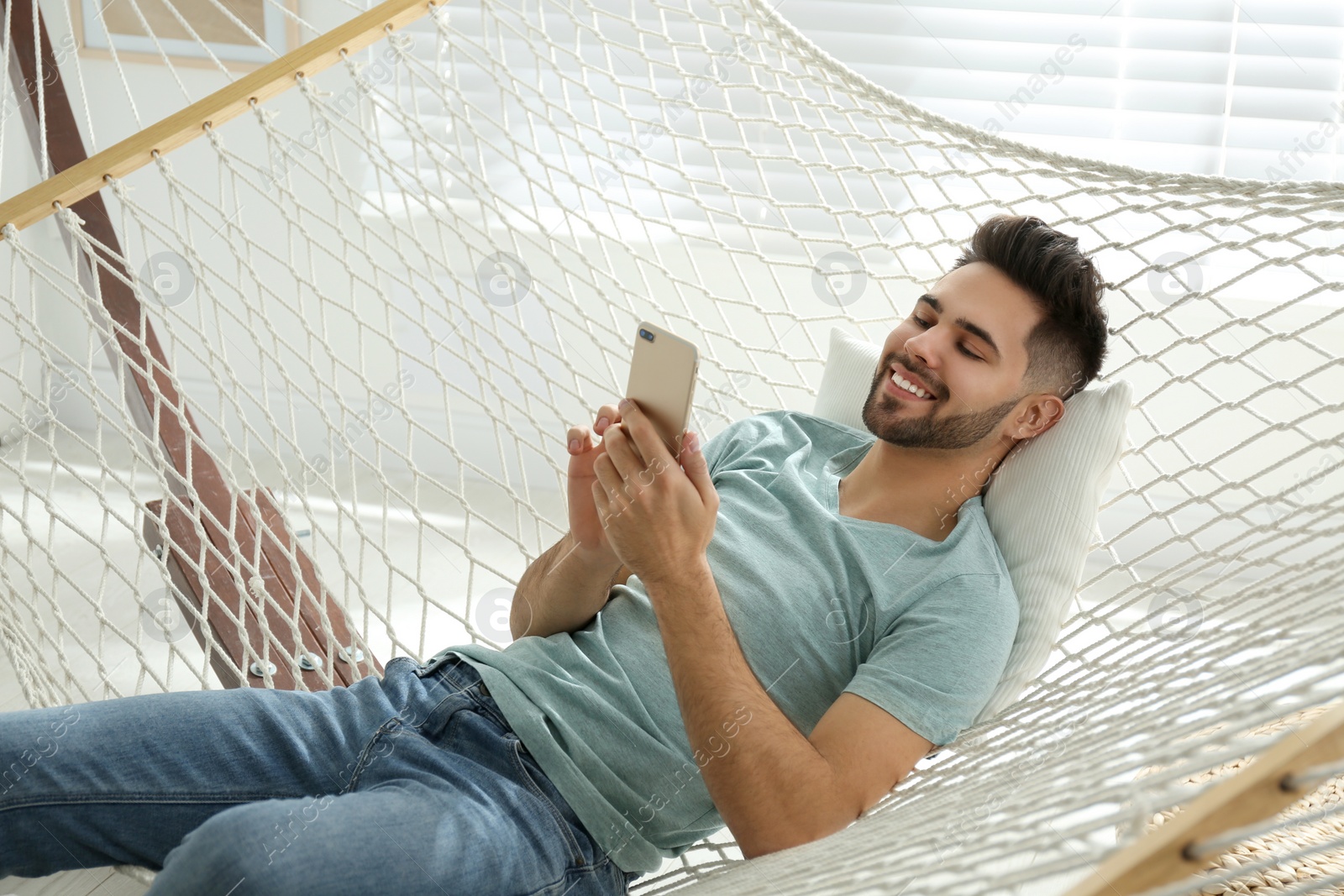 Photo of Young man using smartphone in hammock at home