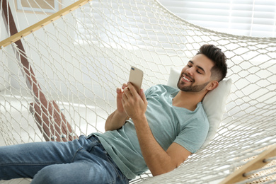 Young man using smartphone in hammock at home