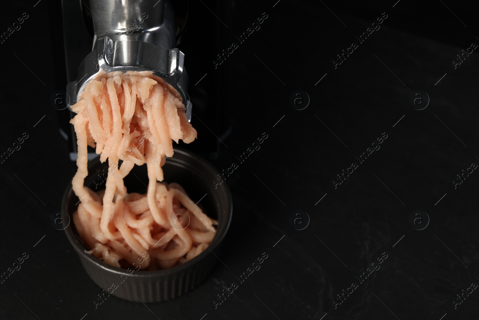 Photo of Electric meat grinder with chicken mince on black table. Space for text