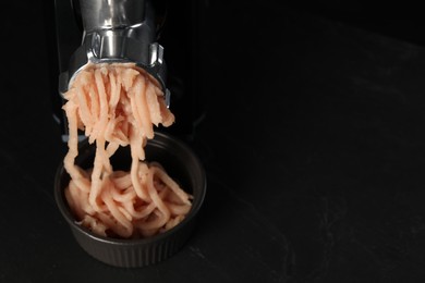 Photo of Electric meat grinder with chicken mince on black table. Space for text