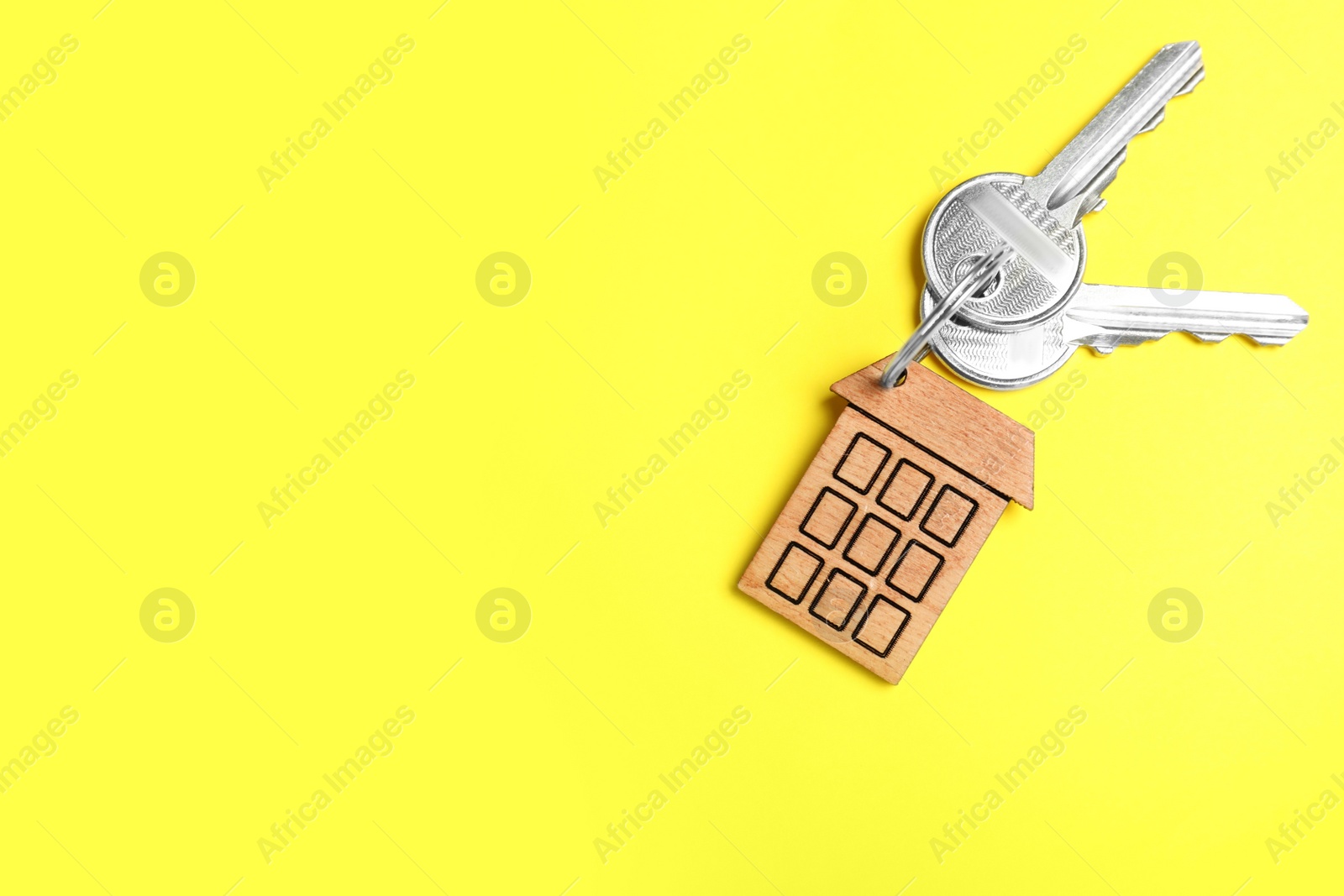 Photo of Keys with trinket in shape of house on yellow background, top view and space for text. Real estate agent services