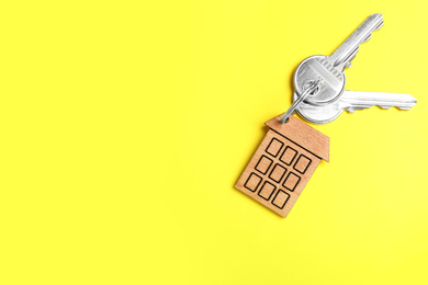 Photo of Keys with trinket in shape of house on yellow background, top view and space for text. Real estate agent services